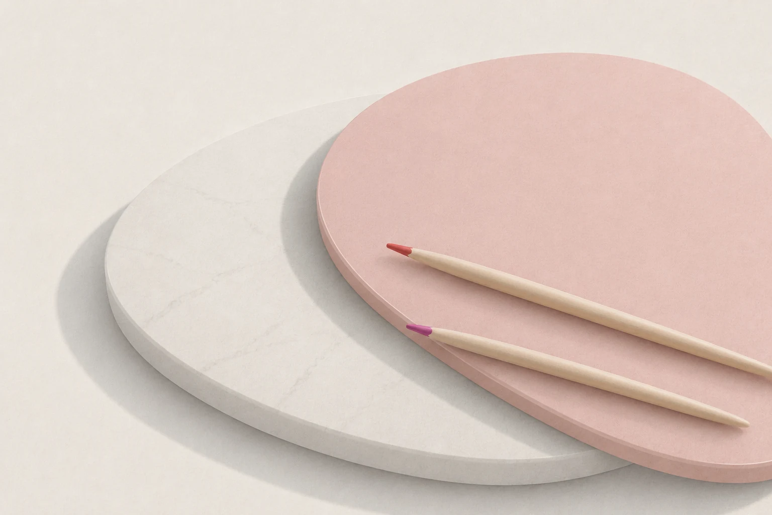 Two pencils resting on soft overlapping paper-like shapes